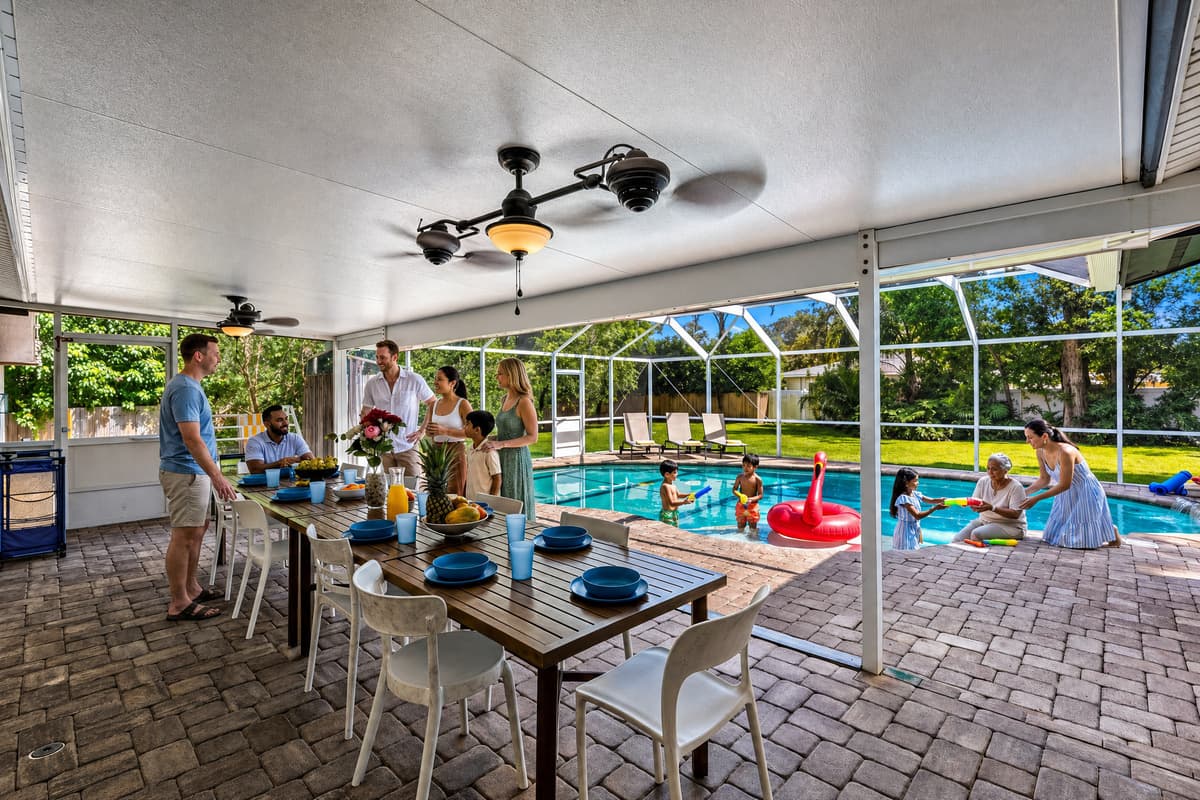 Dinner outside, pool just five steps away. 🏊 The covered lanai seats the whole group under fans, screened from bugs and sun. Kids swim while the table gets set. Evenings here run long — grill, eat, then everyone slides back into the water.