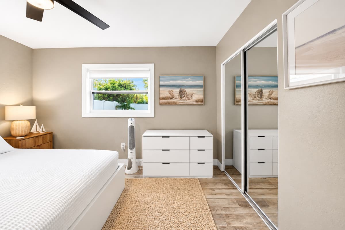 Bedroom featuring a comfortable bed, mirrored closet doors, beach-inspired artwork, and a bright, airy design.