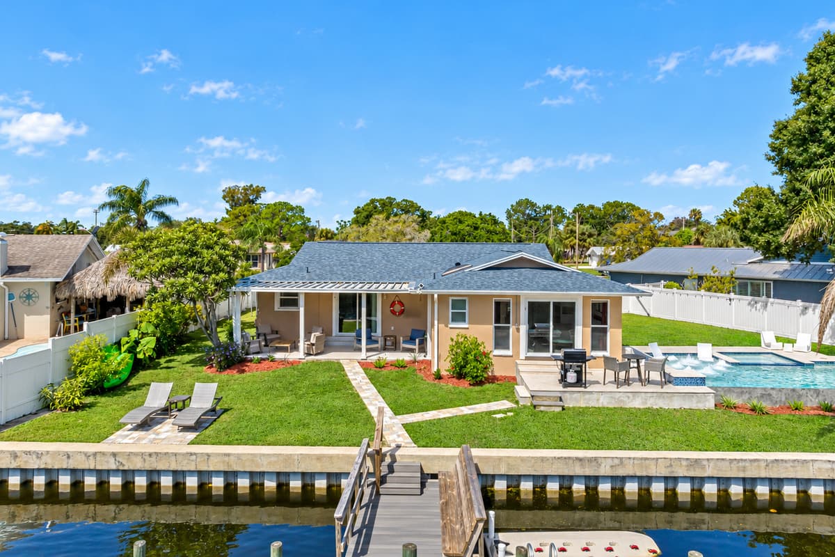 The beautiful back view of this amazing property, showcasing the wonderful swimming pool, access to dock, and the lovely patio area. Make the most of your stay! Book now!