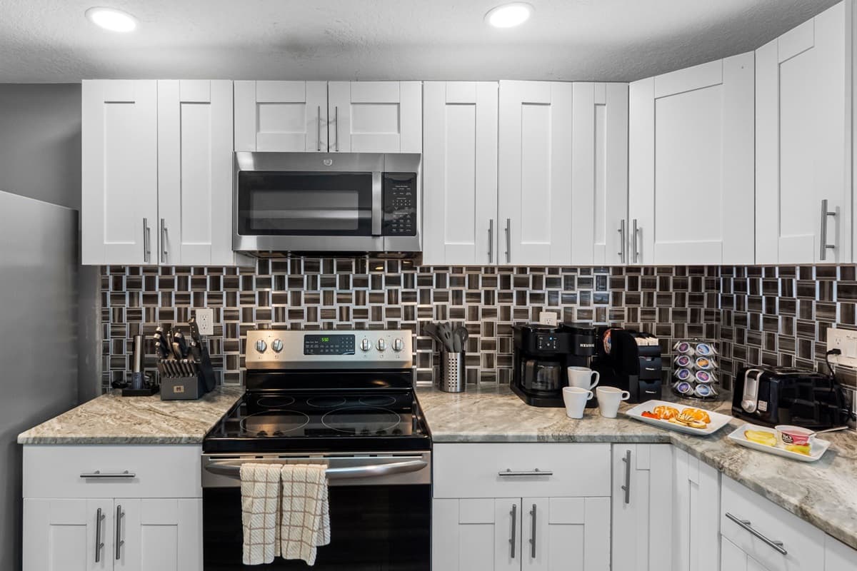 A glossy, geometric backsplash adds a modern flair, complementing the soft tones of the cabinetry and countertops.