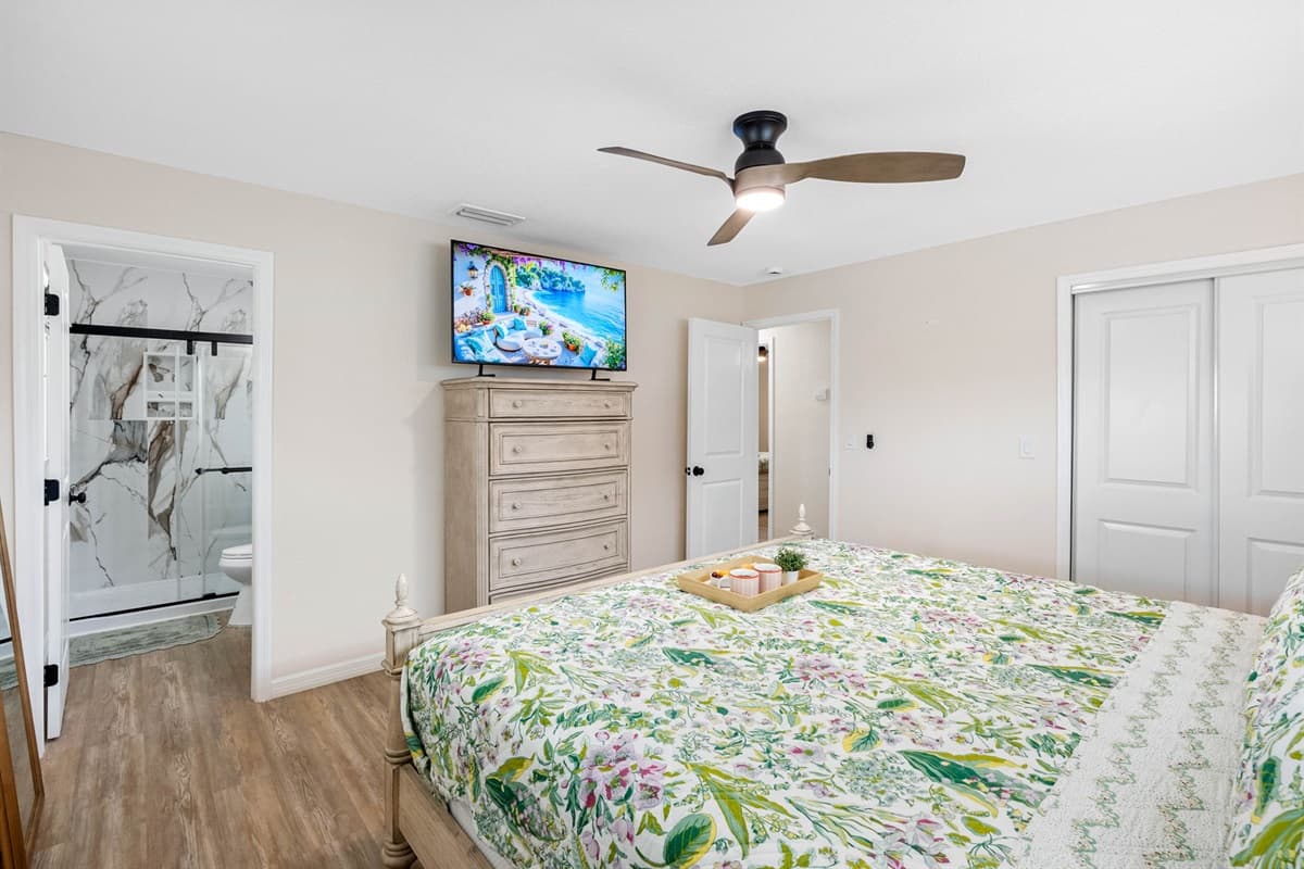 Retreat to this spacious bedroom with a king-size bed, soft botanical bedding, and plenty of natural light. The private ensuite bath features a stunning walk-in shower with marble-style tile.