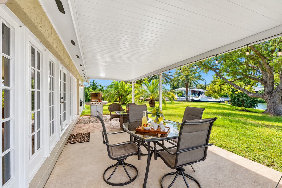 This patio blends indoor comfort with outdoor beauty, featuring a shaded roof, stylish furniture, and a scenic water view.