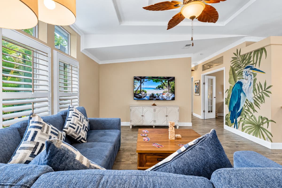 Step into a bright, inviting living room featuring a plush sectional sofa, tropical ceiling fans, and a large smart TV—perfect for family gatherings or cozy nights in.
