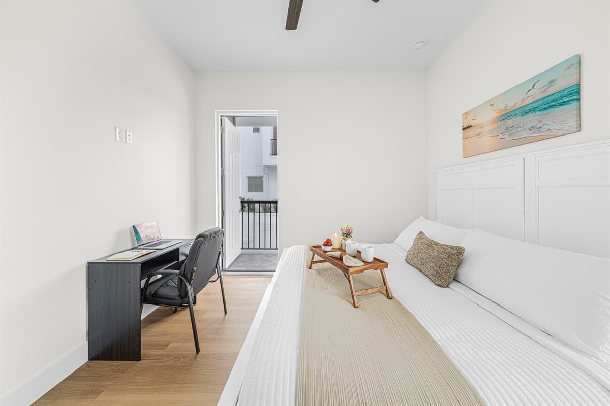 Clean and modern bedroom with a comfortable bed, workspace desk, and balcony access.