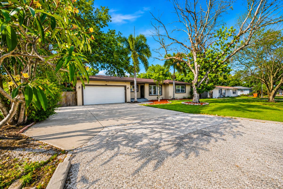 Welcoming driveway entrance framed by tropical plants and mature trees.