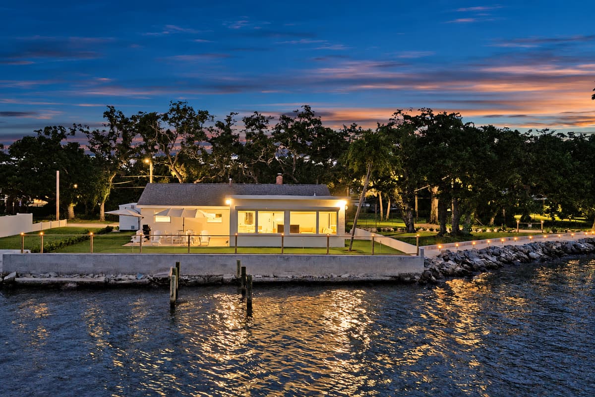 Sunset reflections on the water. Seen from the bay, the home glows behind its seawall as the sky turns pink. This is the view your friends will ask about.