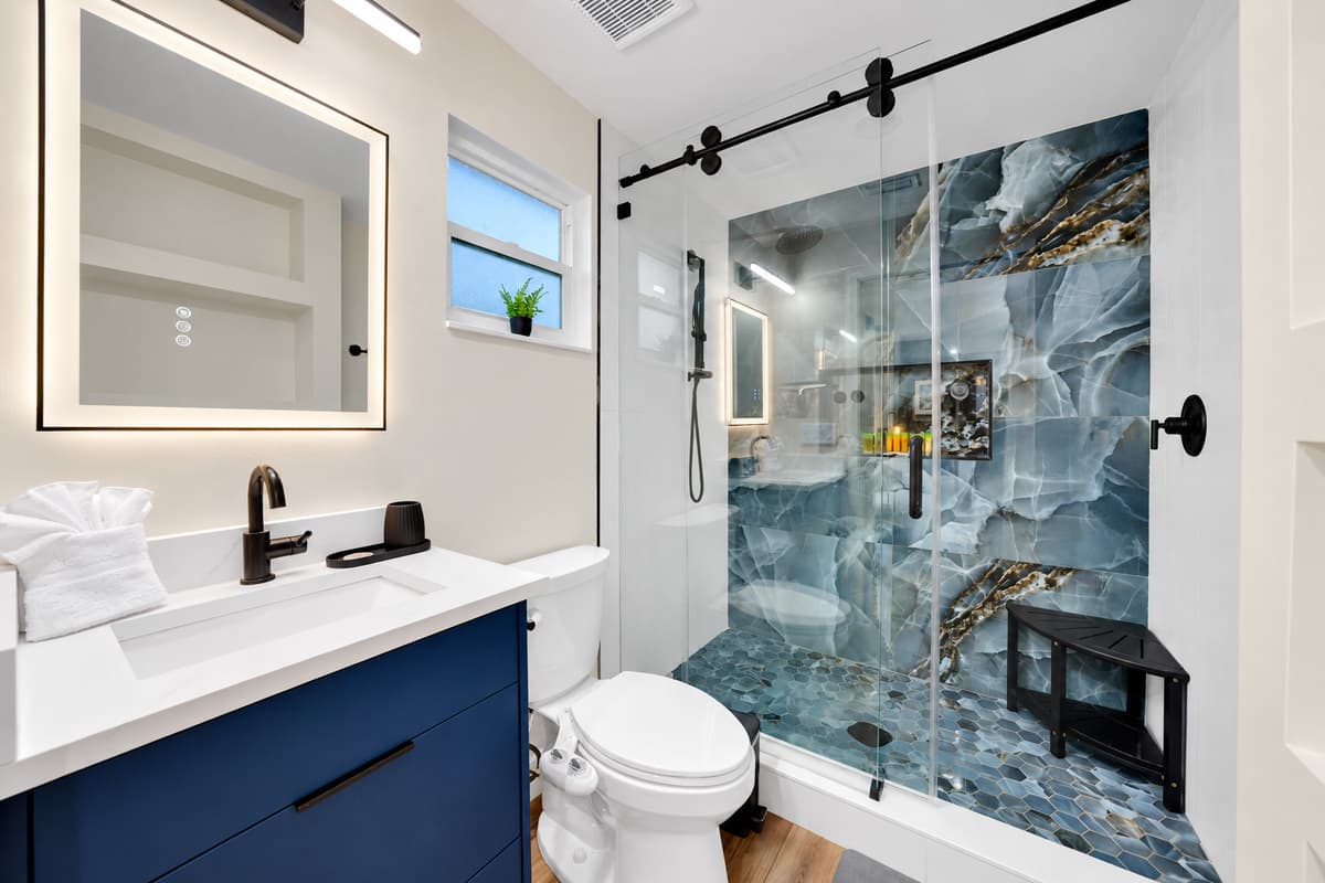 Another full bathroom. Another morning with no queue. Glass walk-in shower, navy vanity with counter space and a wide lit mirror — private, modern and steps from where you're sleeping.