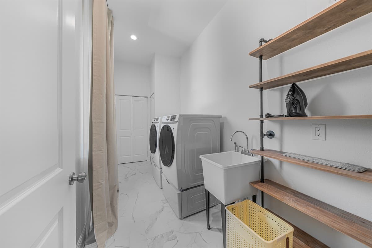Dedicated laundry room with washer, dryer, utility sink, and open shelving for storage.