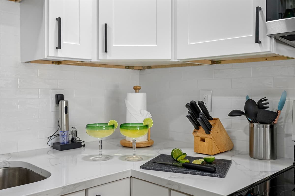 Featuring white shaker-style cabinets with bold black hardware, paired with gleaming marble-style countertops and a clean white subway tile backsplash, this kitchen is as visually stunning as it is functional.