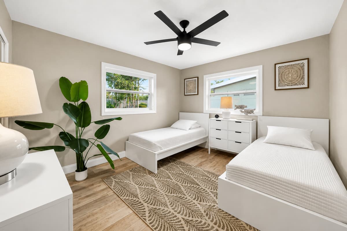 Guest bedroom with two twin beds, neutral décor, ceiling fan, and a dresser positioned between the beds.
