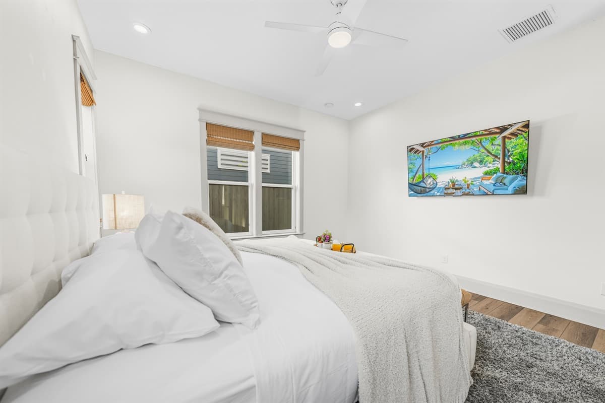 Relax in style — this brand-new bedroom features a wall-mounted smart TV with tropical vibes, ceiling fan, soft bedding, bamboo shades, and warm ambient lighting. Everything you need for a perfect night's rest in Seminole Heights.