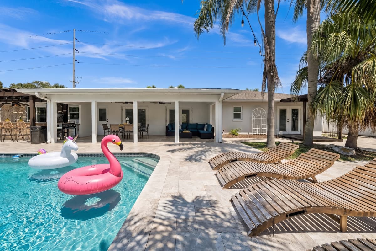 Sparkling pool with flamingo and unicorn floats, sun loungers waiting, and a fully covered lanai beyond, an instant resort escape