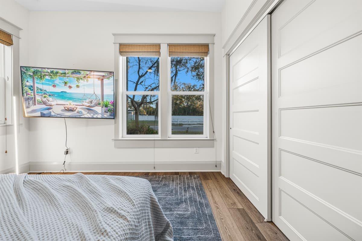 Minimalist-chic bedroom with a white shiplap accent wall, bamboo shades, soft gray duvet, breakfast tray, and warm hardwood floors. Brand-new design meets laid-back Seminole Heights style in every detail.