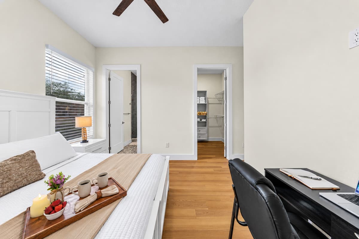 Bright and inviting bedroom with a comfortable bed, workspace desk, and easy access to nearby rooms—perfect for both relaxation and productivity.