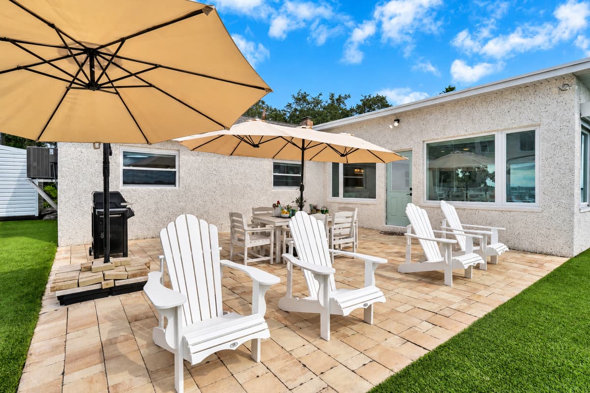 Adirondacks, umbrellas and sunshine. Multiple Adirondack chairs, a dining table under umbrellas and a gas grill, all on a sunny paver patio. Your outdoor living room.