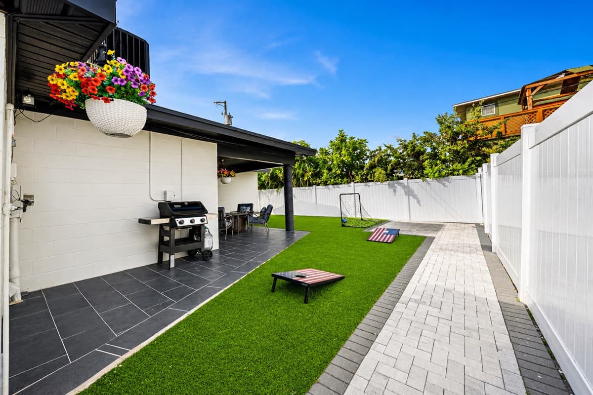 Full backyard overview with BBQ grill, cornhole, and private fenced-in yard.