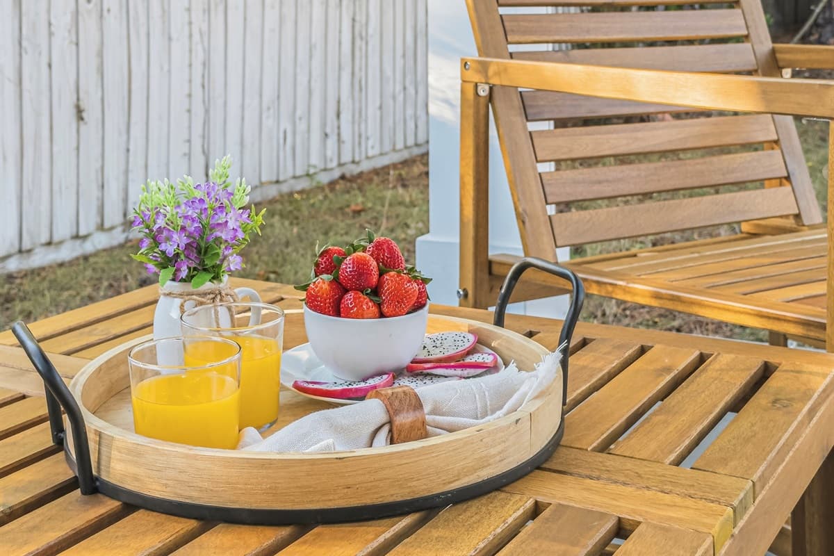 Al fresco mornings done right — a tray of fresh strawberries, orange juice, and flowers set on the outdoor wood patio chair. This brand-new Seminole Heights home is your personal Florida paradise from day one.