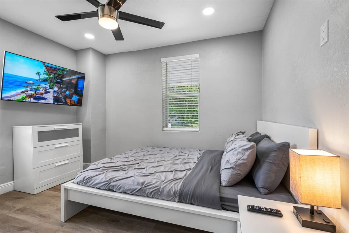 Bedroom 1 — queen bed with fresh linens, wall-mounted TV, nightstands, and a ceiling fan for a restful night's sleep.