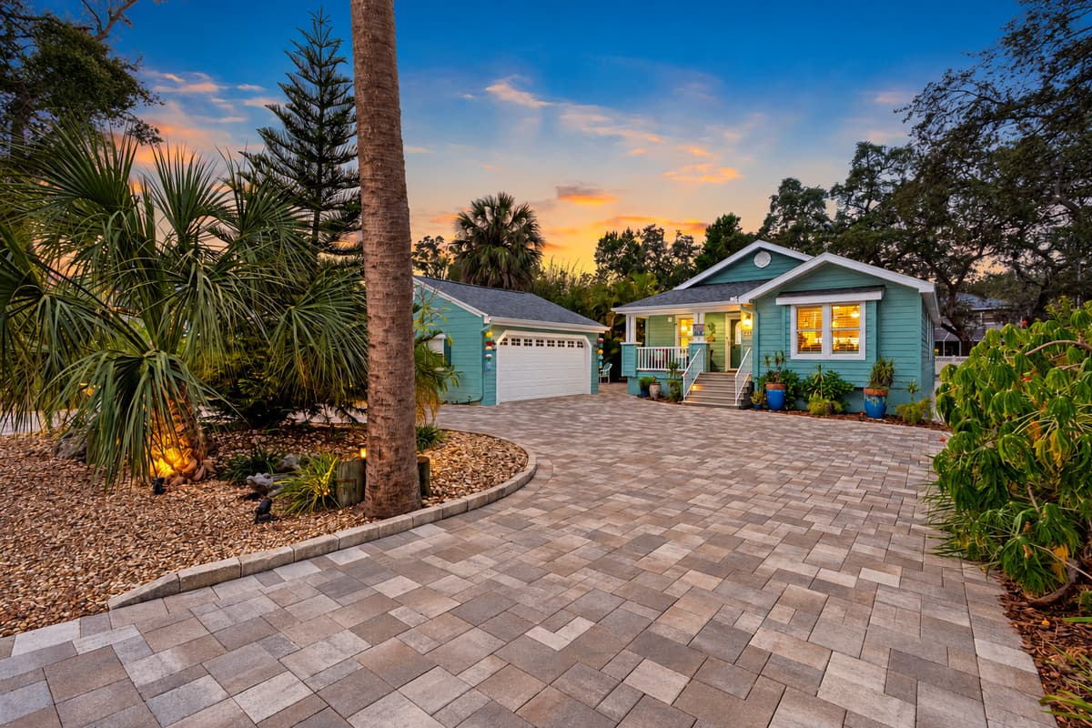 The expansive driveway leads to a charming cottage-style home with lush greenery and inviting exterior design.