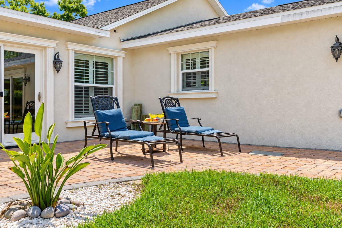 Two inviting chaise lounges with plush cushions sit against the home’s exterior, offering a peaceful spot for sunbathing or enjoying a cool drink.