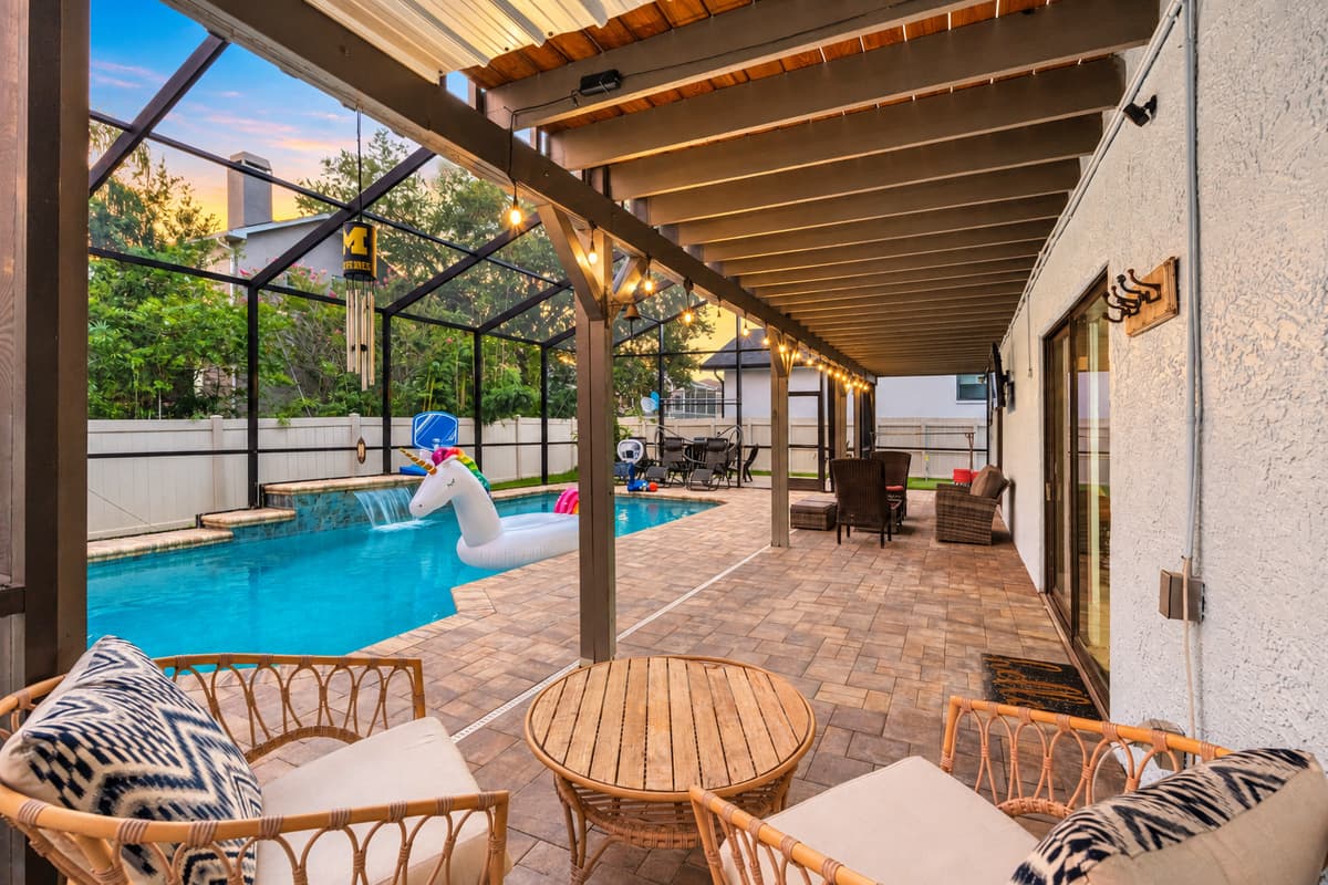 This fully screened backyard retreat features a sparkling pool, playful floaties, cozy conversation areas, and string lights that make evenings feel magical.