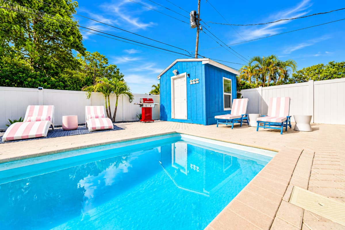Relaxing poolside retreat with cushioned loungers, privacy fencing, and a bright blue pool house accent.
