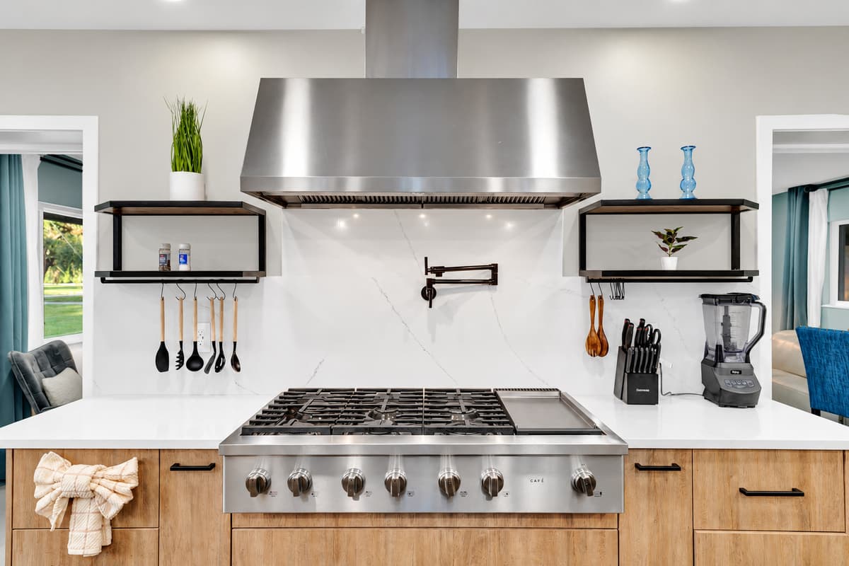 Pot filler over a six-burner range. Enough said. Professional cooktop, full hood and knives within reach — cook a proper meal for the whole house without carrying a single heavy pan.