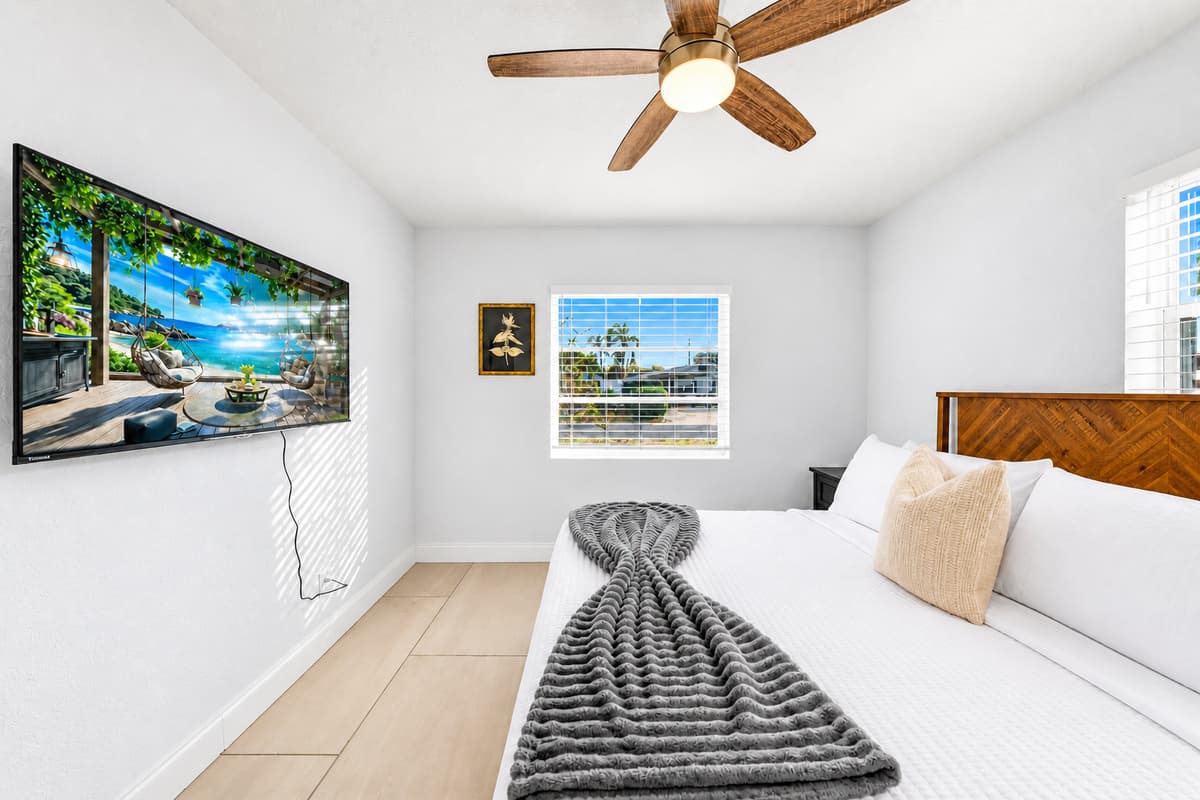 Bedroom 2 featuring a cozy queen bed, wall-mounted TV, and bright natural lighting.