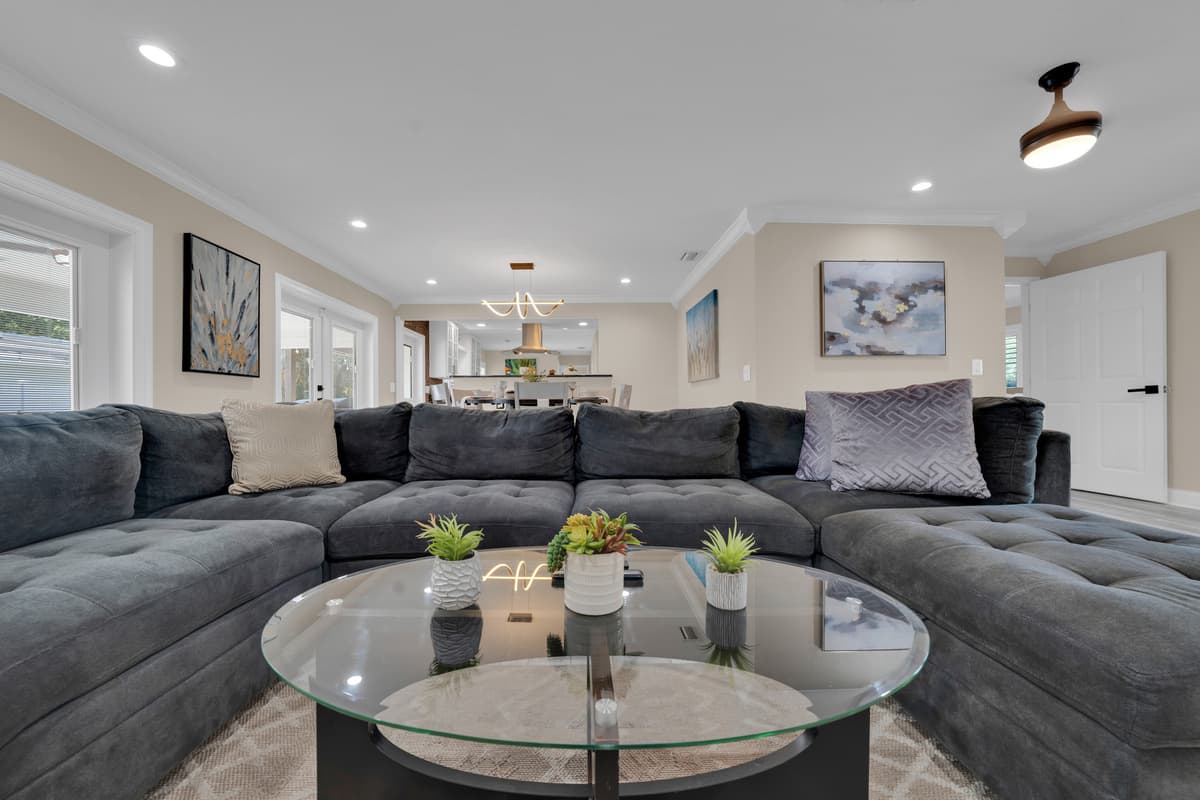 006-A plush gray sectional wraps around a glass coffee table in a bright, symmetrical living room built for the whole group to gather