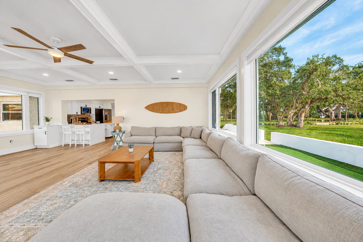 Lounge with views of oaks and water. The sectional wraps around the room under coffered ceilings, with windows to the lawn and bay. Space to spread out and relax.