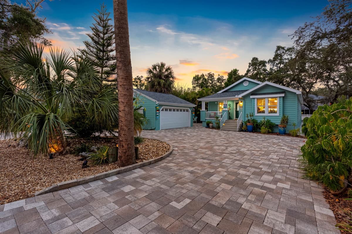 The expansive driveway leads to a charming cottage-style home with lush greenery and inviting exterior design.