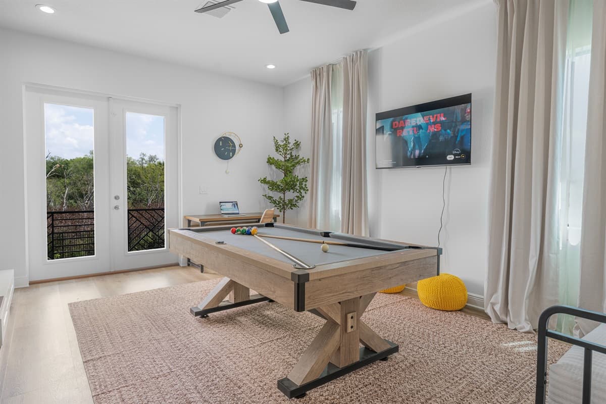 Bright and inviting game space with pool table, TV, and access to outdoor balcony views.