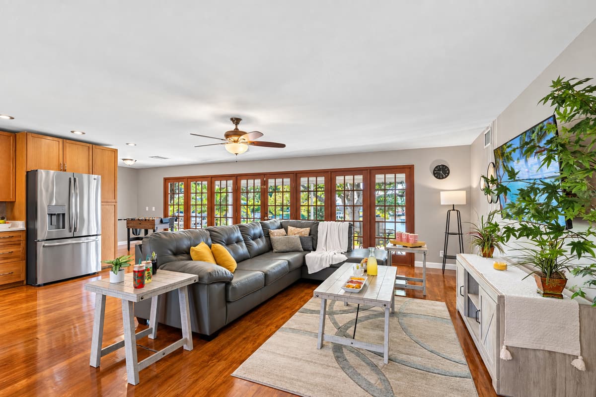 This open-concept living room welcomes you with floor-to-ceiling French doors that flood the space with natural light. The sleek leather sectional, soft gray tones, and pops of yellow accents create a cozy yet modern retreat.