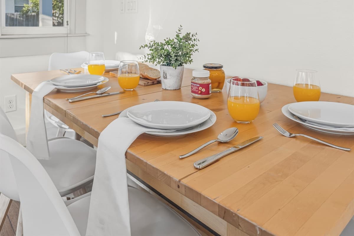 Dining done beautifully — the farmhouse table set with white plates, fresh OJ, linen napkins, and a potted centerpiece. Every breakfast, lunch, and dinner feels like an occasion in this brand-new Seminole Heights home.