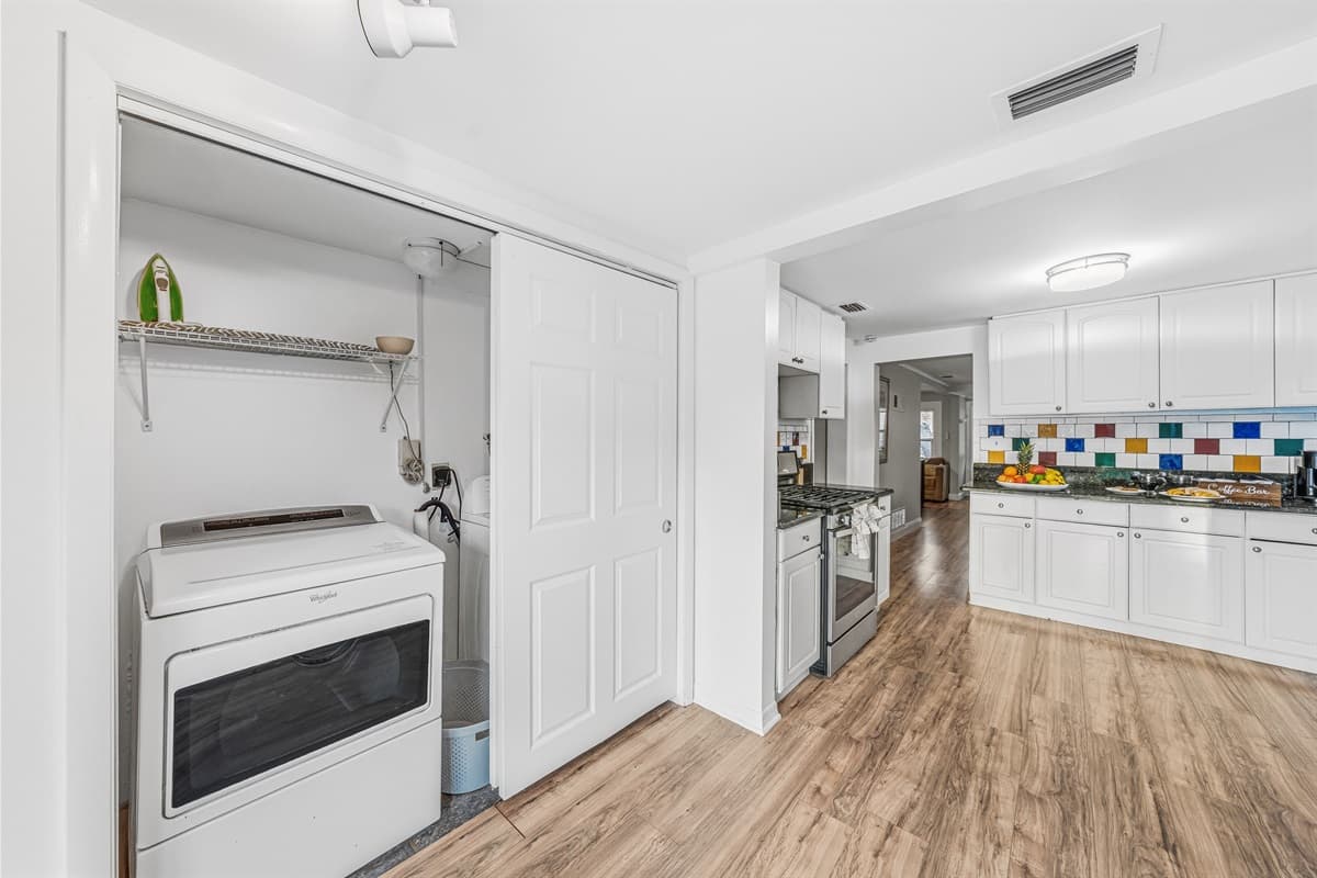 Open kitchen and laundry layout with modern flooring and colorful backsplash.