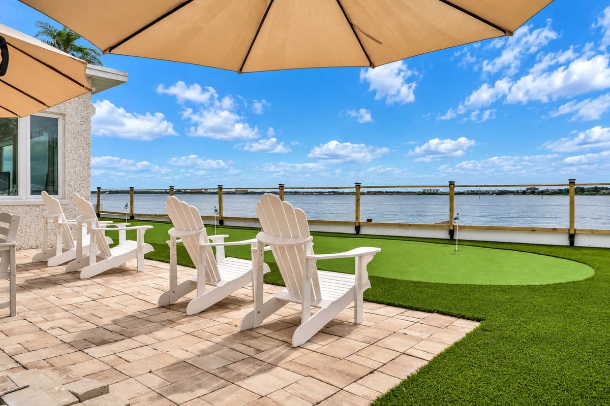 Chairs lined up for sunset. Adirondack chairs face the water across the paver patio and putting green. Grab a seat early, the show is worth it.