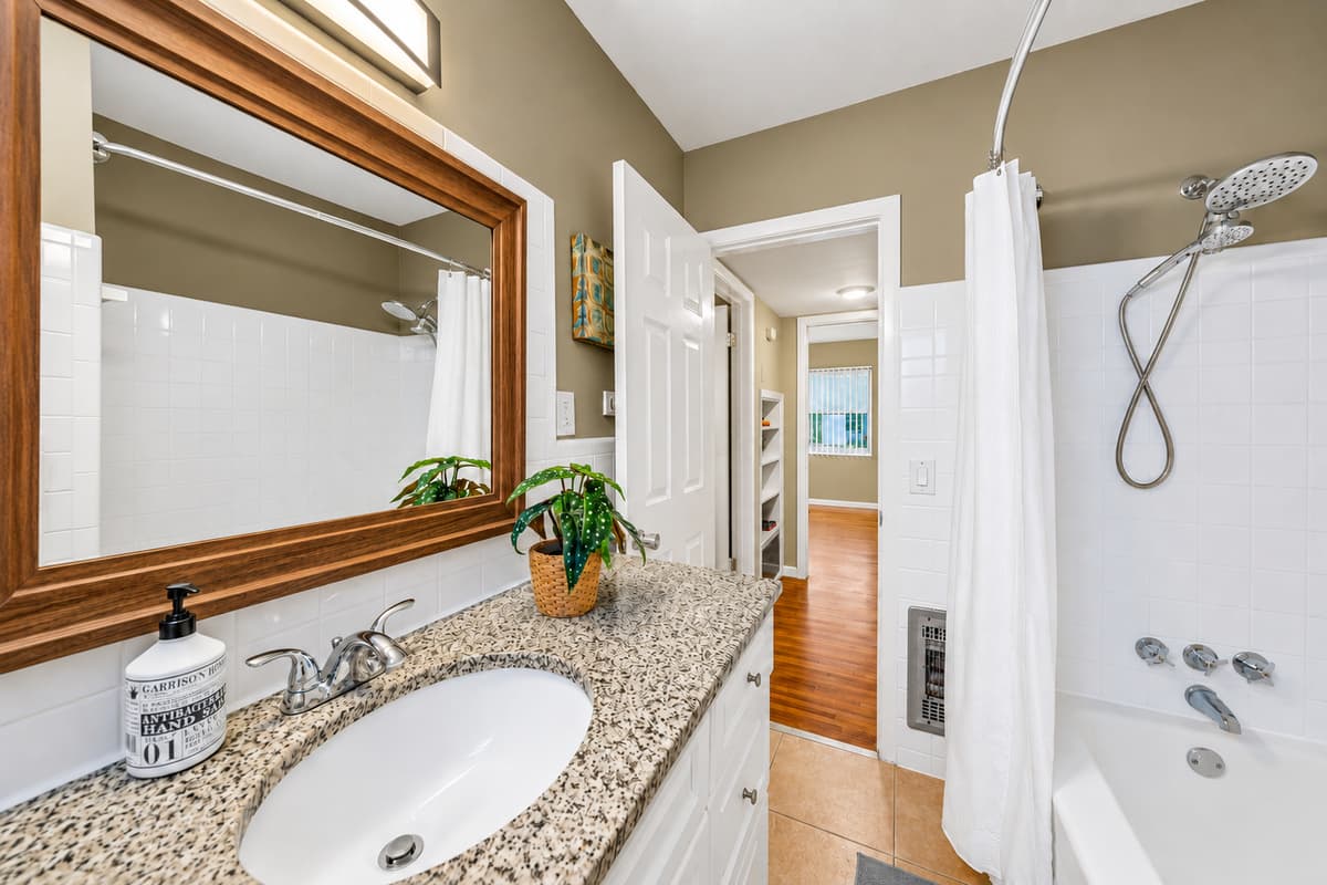 Clean and inviting second bathroom with granite countertops, framed mirror, and shower/tub combination.