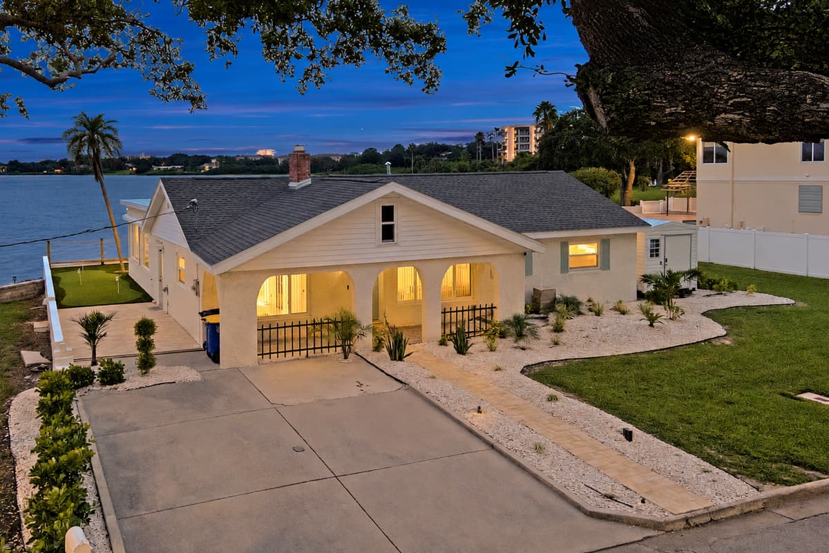 Lights on, porch glowing, you're home. The front of the house glows at dusk with arched porch lights and landscaped walkways. A warm welcome after dinner out or a long drive.
