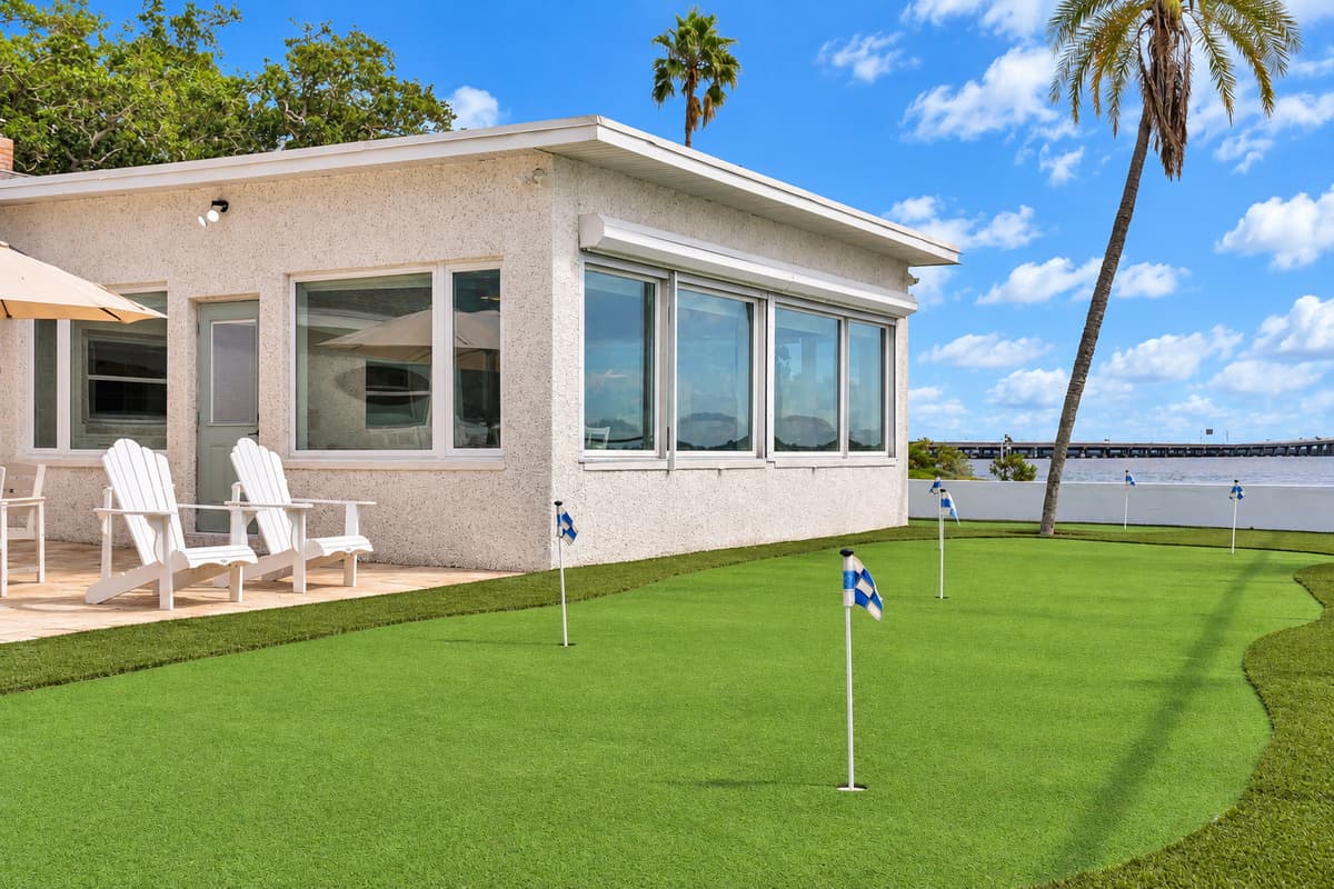 Golf outside the sunroom windows. Adirondack chairs sit beside the sunroom, facing the putting green and bay. Relax inside or out with the same view.
