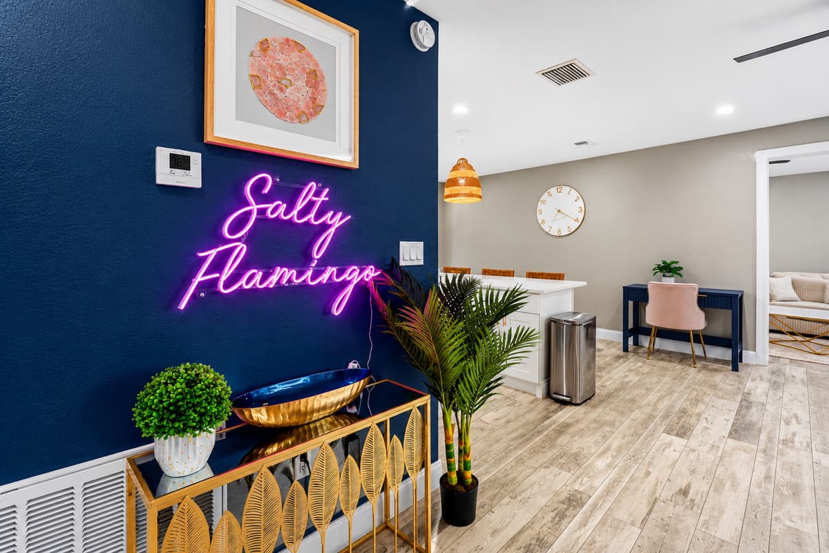 Stylish entry and dining area featuring a blue accent wall, neon "Salty Flamingo" sign, and modern coastal décor.