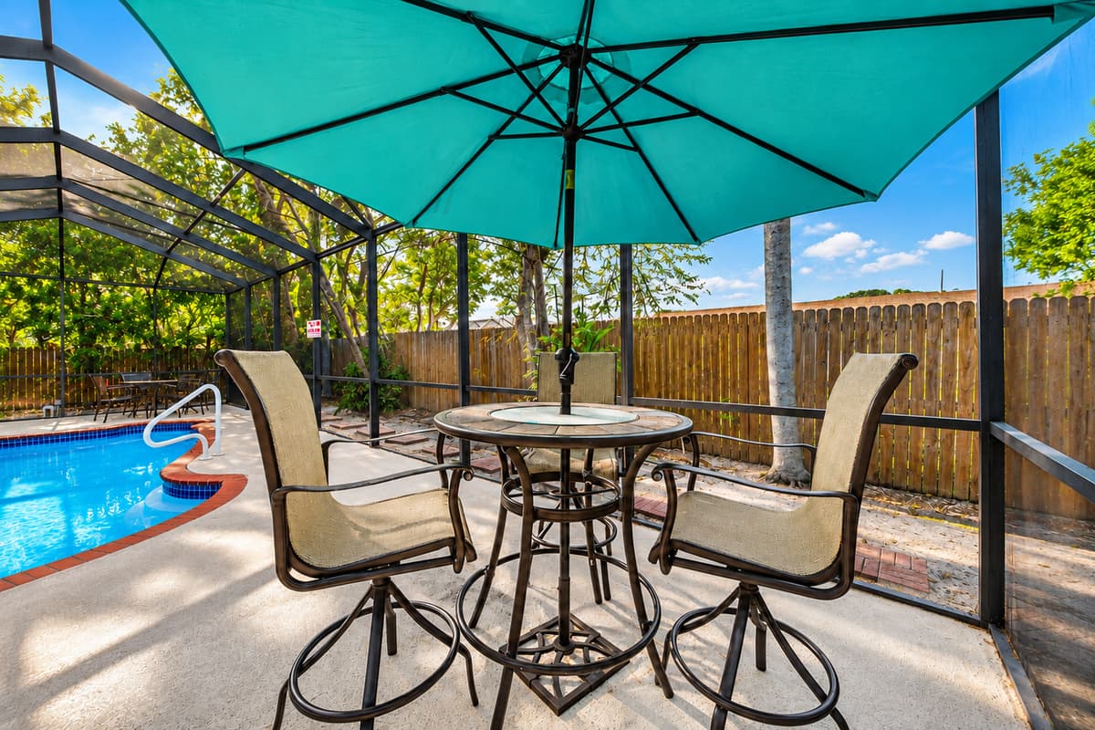 Outdoor dining space with umbrella seating overlooking the screened pool area.