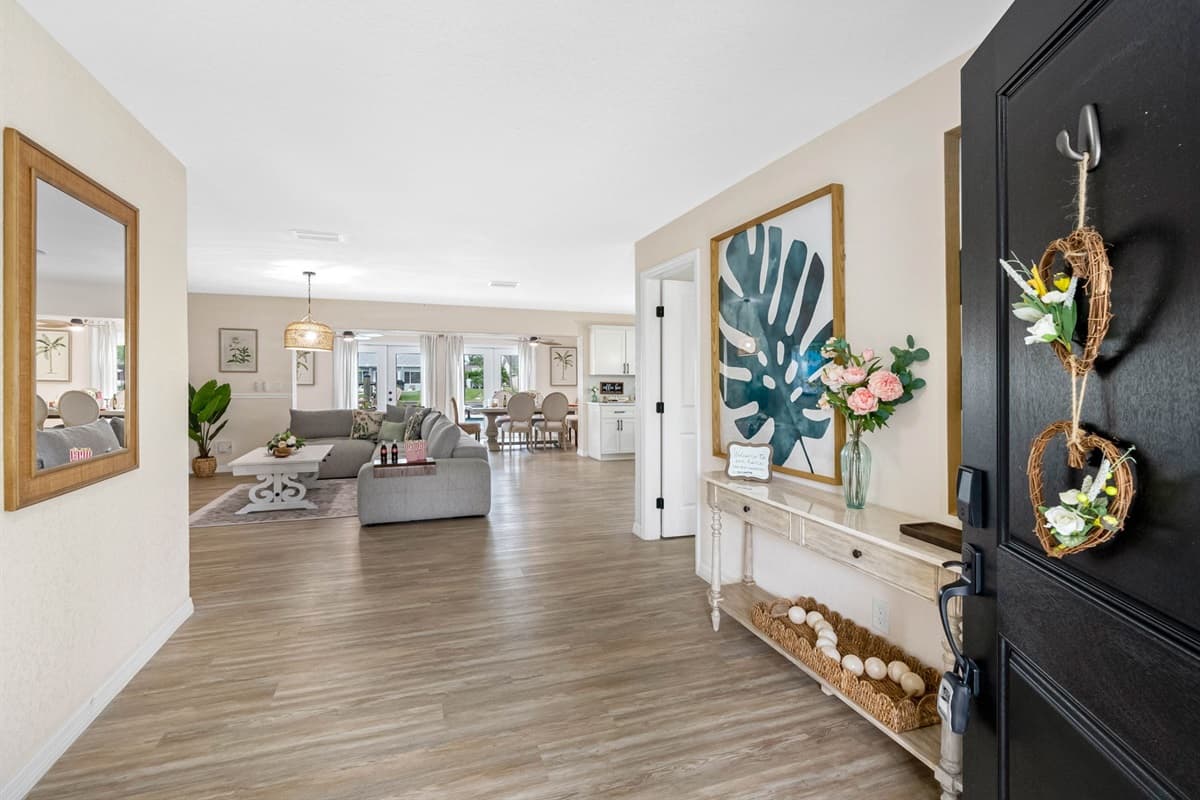 Bright French doors lead to the sun-soaked patio, framed by a cozy corner with a natural wood chair, leafy plant, and soft floral rug — the perfect spot to pause before stepping outside.