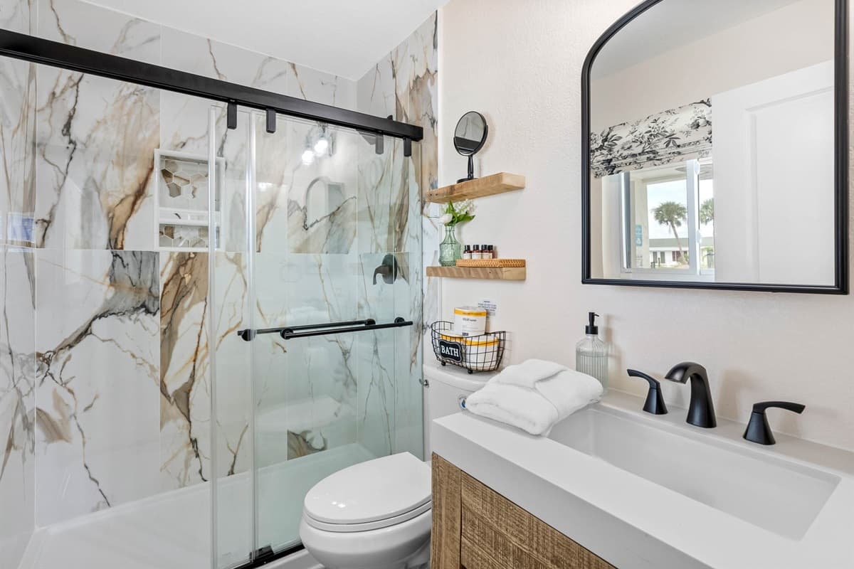 Step into this stylish bathroom featuring a striking marble-style walk-in shower with black-framed glass doors, a chic vanity, and matte black fixtures for a bold, modern look.