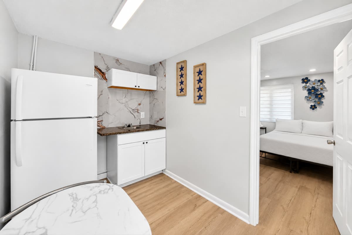 Studio suite kitchenette area featuring a refrigerator, sink, cabinets, and dining table for two, perfect for added convenience and independence.