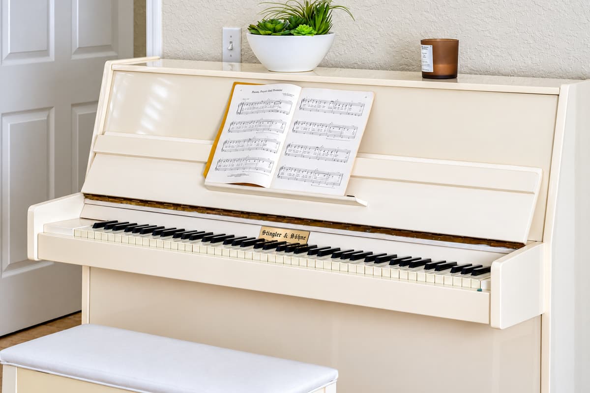 A sleek ivory upright piano with an open music book, topped with a potted plant and candle for a touch of charm.