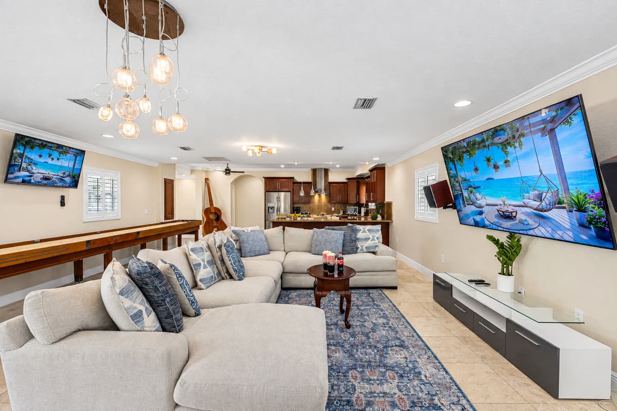 This inviting living space blends modern design with cozy comfort, featuring a plush sectional sofa, two large wall-mounted TVs, and a sleek entertainment console.