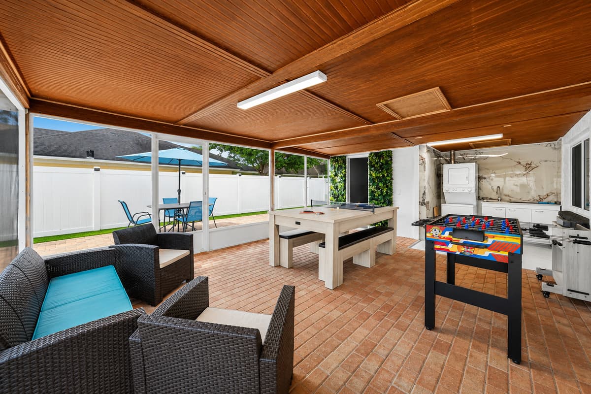 Covered outdoor entertainment area featuring comfortable seating, a pool table, foosball table, and plenty of space for family fun and relaxation.