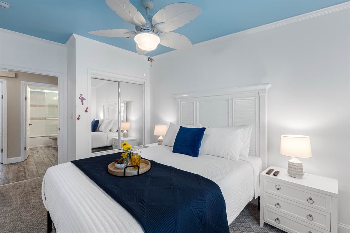 This bright and inviting bedroom features a queen bed with crisp white linens and a calming navy accent blanket.