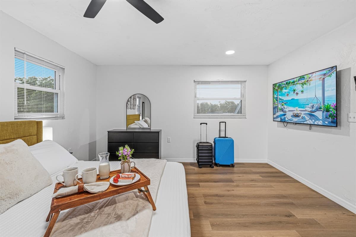 Large bedroom with king bed, wall-mounted TV, and plenty of space for relaxation and comfort 
Tray and food setup shown are for staging purposes only and are not included.