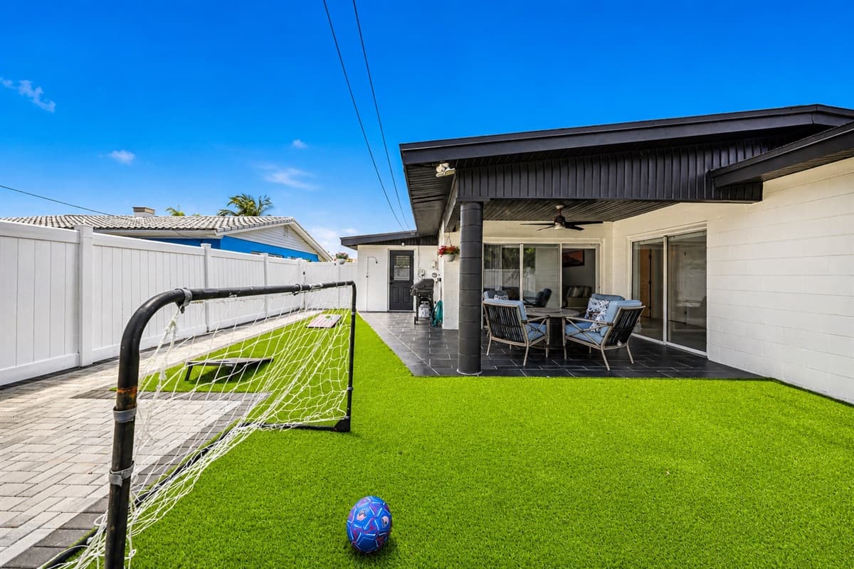 Bright and open backyard area with artificial grass, soccer goal, and patio access.
